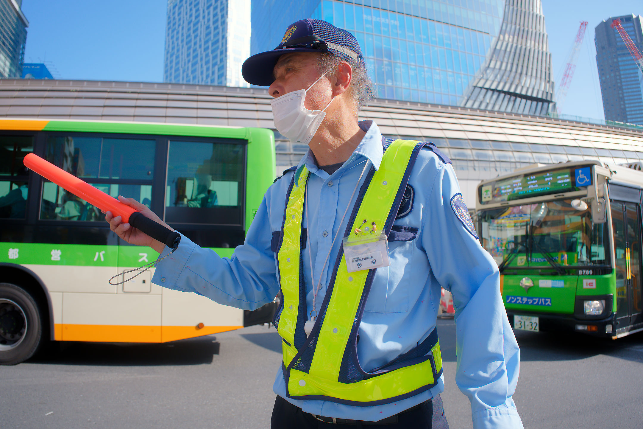 an elderly man in front of two buses conducting bus traffic at shibuya station
